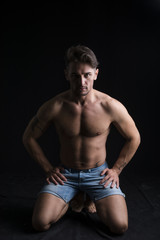 Fototapeta na wymiar Handsome shirtless muscular man on his knees on dark