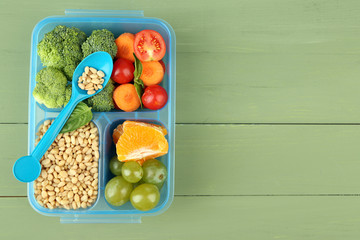 Tasty vegetarian food in plastic box on green wooden table