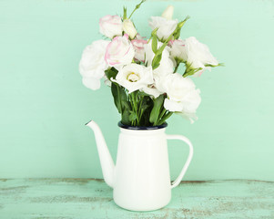 Beautiful eustoma flowers in teapot, on wooden background