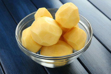 Raw peeled potatoes in glass bowl  on color wooden background