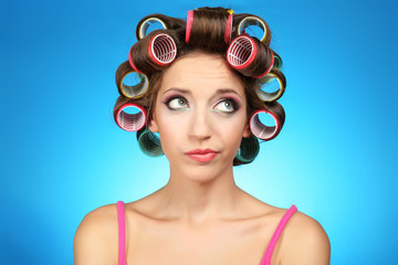 Beautiful girl in hair curlers on blue background