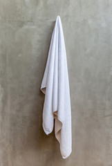 The white towel is hanging on a hanger with concrete wall in the