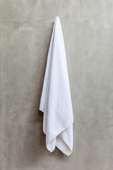 Fototapeta premium Hanging white towel draped on exposed concrete wall in the bathr