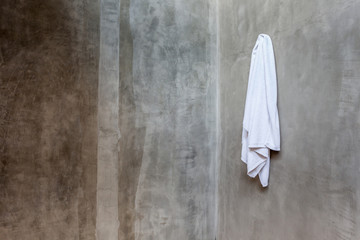 Naklejka premium Hanging white towel draped on exposed concrete wall in the bathr