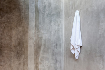 Obraz premium White towel is hanging on the exposed concrete wall in the bathr