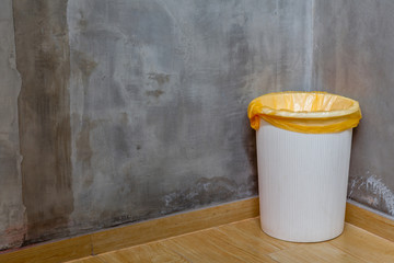 The white can bin at the corner on wooden floor with exposed cem