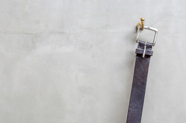 The black leather belt hanging on the hanger with exposed concre