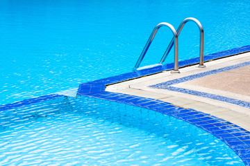 A view of curved light clear blue swimming pool with steel ladde