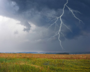 Thunderstorm with lightning in meadow. Dark ominous clouds.