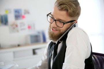 Young designer in office talking on phone