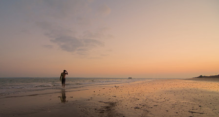 Fototapeta na wymiar A single surfer on the shore, with the sun setting behind him
