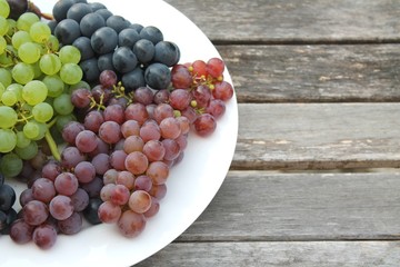 Colorful grapes on a white plate on a rustic wooden table