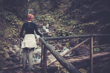 Hiker with hiking poles  walking over wooden bridge in a forest