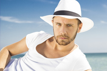 Man on beach looking to camera wearing hipster summer hat.