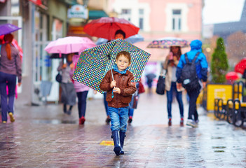cute boy with umbrella walking on crowded city street