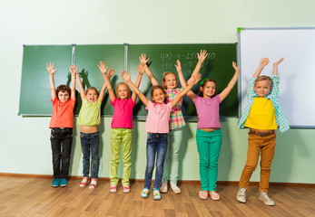 Kids stand with arms up in line near blackboard