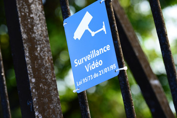 Blue sign of video surveillance fastened to metallic fence