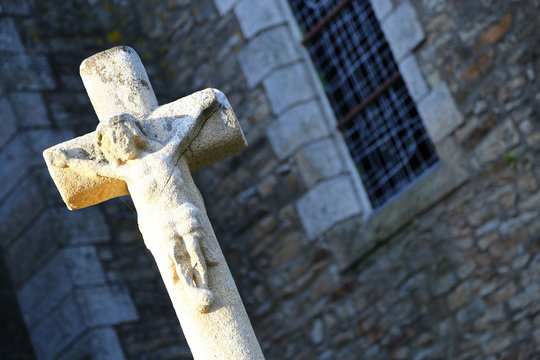 Closeup to stone cross statue in front of an old building