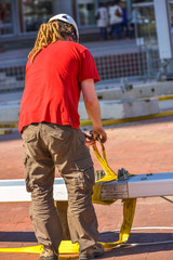 A construction worker with long dreadlocks fastening a yellow ho