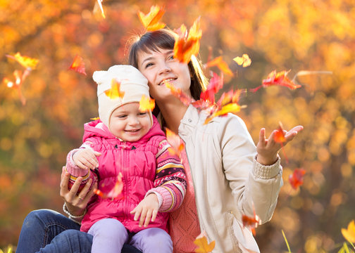 Kid and beautiful mother play and throw leaves outdoor in autumn