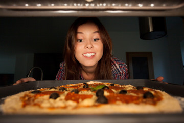 Happy girl putting pizza into oven