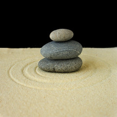 Fototapeta na wymiar Three stones lying on sand with circular pattern, black backgrou