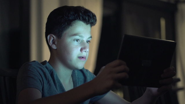 Young teenager playing game on tablet computer at night