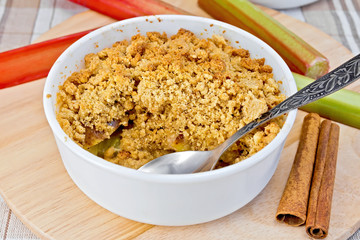 Crumble with rhubarb in bowl on linen tablecloth and board