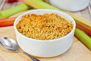 Crumble with rhubarb in bowl on tablecloth and board