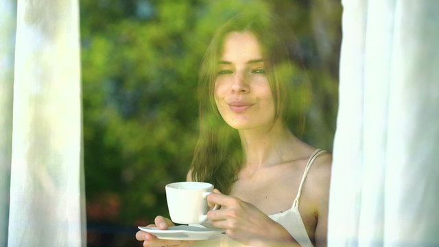 Pretty woman drinking coffee by the window in the morning