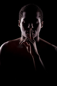 frican man with the face in the shadow holding finger on lips
