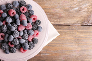 Iced berries on plate, on wooden background