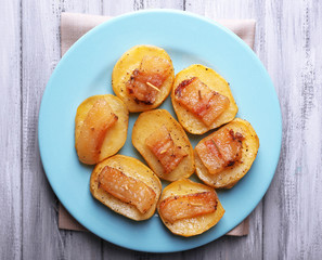 Baked potato with bacon on plate, on wooden background