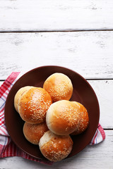Tasty buns with sesame on plate, on color wooden background