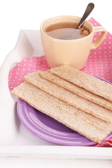 Crispbreads on plate and cup of tea on wooden tray close up