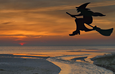 Witch flying on broomstick at dawn near sandy beach