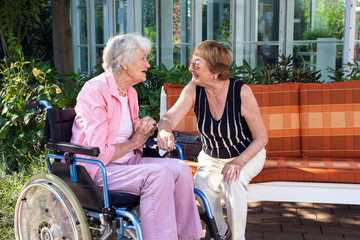 Two senior ladies chatting on a garden bench.