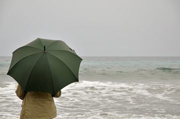 woman with green umbrella on the beach on a rainy day
