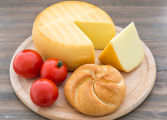 Smoked cheese wheel, tomatoes and bread on wooden table