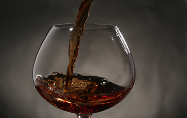Naklejka na ściany i meble Red wine pouring into wine glass, close-up