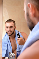 Obraz premium Young man shaving his beard in bathroom