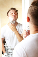 Young man shaving his beard in bathroom