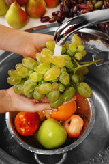 Woman's hands washing grapes and other fruits in colander in