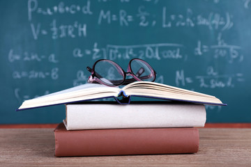 Books and glasses on wooden table on blackboard background