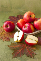 apples in a basket on a table strewn with autumn leaves