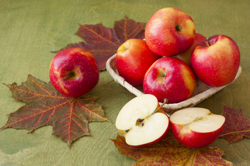 apples in a basket on a table strewn with autumn leaves