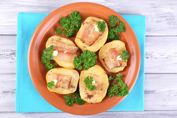 Baked potato with bacon on plate, on wooden background