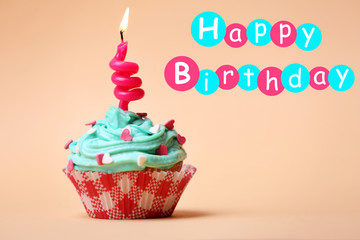 Delicious birthday cupcake on table on beige background