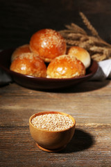 Tasty buns with sesame on plate, on wooden background