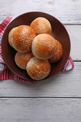 Tasty buns with sesame on plate, on color wooden background
